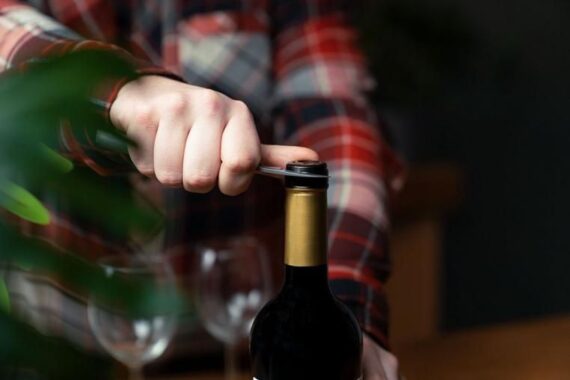 Main découpant la capsule d’une bouteille de vin avec un couteau